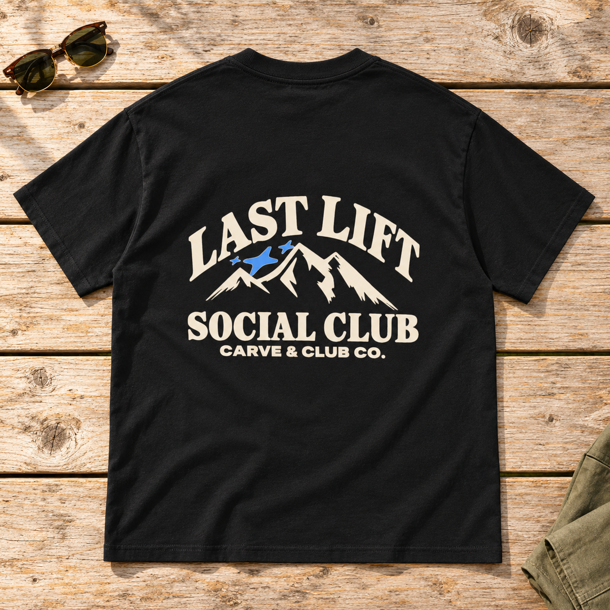 Last Lift Social Club Tee — back view flat lay on wood tabletop