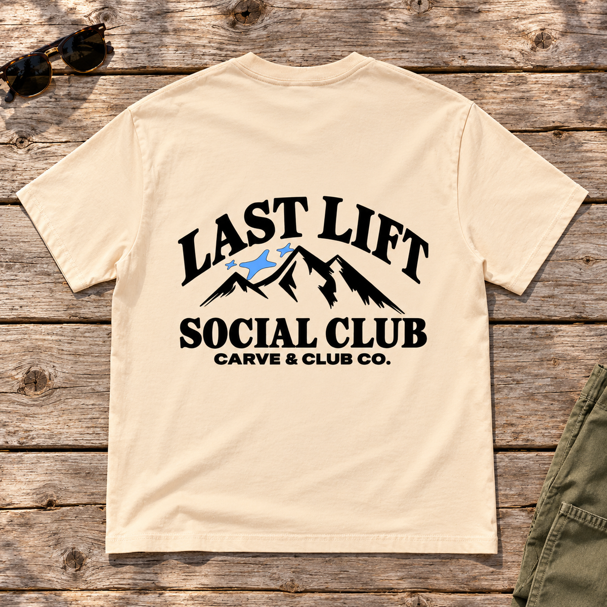Last Lift Social Club Tee — back view flat lay on wood tabletop