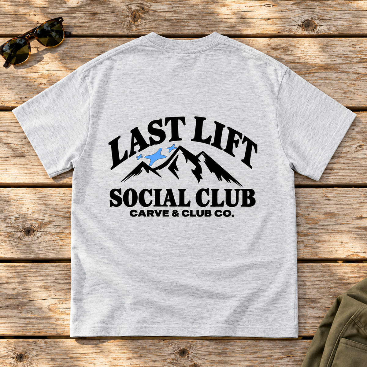 Last Lift Social Club Tee — back view flat lay on wood tabletop