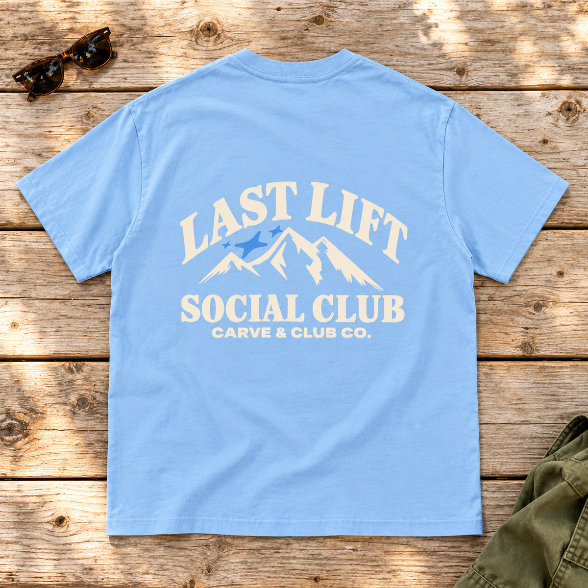 Last Lift Social Club Tee — back view flat lay on wood tabletop